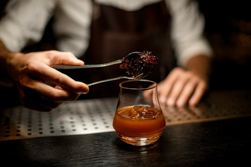 Bartender adding chilled melting caramel with twezzers to the cocktail glass with ice cubes