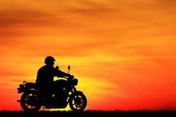 Silhouette biker with his motorbike beside the natural lake and beautiful sunset sky.