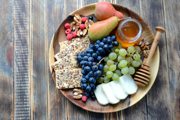 Wine snacks on a wooden platter: cheese, nuts, crackers, pears