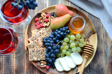 Red wine in glasses and snacks for wine on a wooden platter: cheese, nuts, crackers, pears, honey, grapes