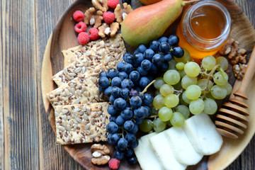 Wine snacks on a wooden platter: cheese, nuts, crackers, pears