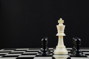 Perseverance in the face of a challenge, a conceptual image of a lonely white coloured king standing on a chessboard surrounded by all the black chess pieces.