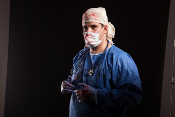 Side view portrait of crazy doctor with blood on his coat looking at the camera