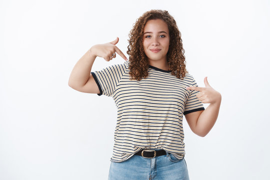 Proud confident cool stylish european plump curly-haired attractive girl smiling bragging own accomplishments showing herself assertive pointing index fingers body smirking delighted