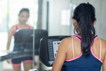 Fototapeta premium Young woman practicing in the gym with mirrors. Girl running on treadmill at fitness club.