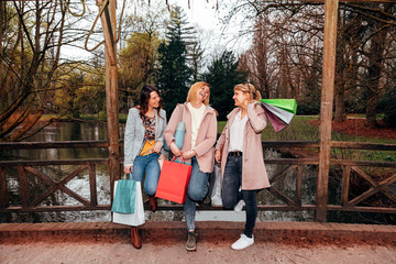 three female friends carrying shopping bags, talking, laughing and joking together on a bridge in...