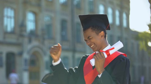 Cheerful male dancing celebrating graduation outdoors university, knowledge