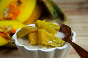 Top view pumpkin in sweet coconut milk in white bowl and wooden spoon with fresh slide pumpkins on bamboo tray background.