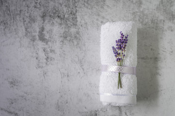 Twisted bath towel with lavender on light gray background. Minimalism, soft focus, copy space. SPA concept.