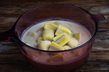 Delicious banana in coconut milk in glass pot, Thai traditional dessert on wooden table background.