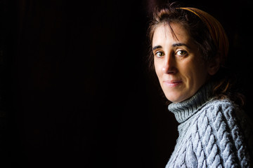 woman on the side with a black background, wearing a gray wool sweater and a ribbon in her hair