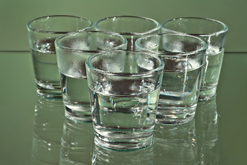 Alcoholic drink in clear glasses. Little cups isolated on green background. Frozen drinks on glass table.