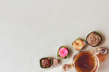 Thai sweets in banana leaves and a cup of tea that are arranged on paper background.  Top view image.