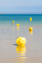 Five large yellow buoys lying on the wet sand and floating on the sea, delimiting a launching channel for small boats on the beach in Penvenan, Brittany, France, under a bright sunshine.