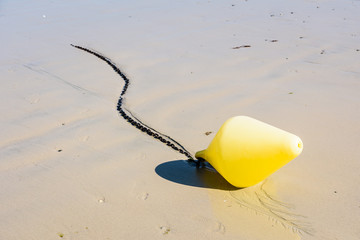 Close-up view of a large yellow buoy and its anchorage chain, used as a launching channel marker, lying on the wet sand on the beach in Penvenan, Brittany, France, under a bright sunshine.