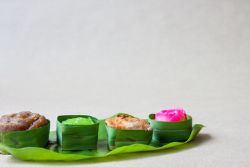 Thai sweets in banana leaves that are arranged on leaf with brown paper background.