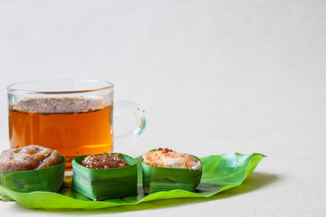 Thai sweets in banana leaves and a cup of tea that are arranged on leaf with brown paper background.
