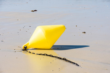 Close-up view of a large yellow buoy and its anchorage chain, used as a launching channel marker, lying on the wet sand on the beach in Penvenan, Brittany, France, under a bright sunshine.