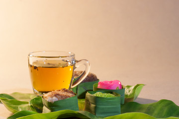 Thai sweets in banana leaves and cup of tea that are arranged on leaf with brown paper background.