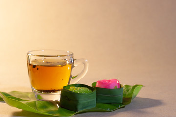 Thai sweets in banana leaves and cup of tea that are arranged on leaf with brown paper background.
