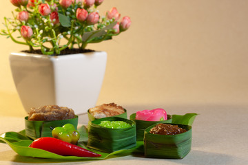 Thai sweets in banana leaves that are arranged with flower on paper background.