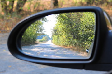 Car mirror with image of summer forest in reflection in good clear weather as popularization of automotive tourism