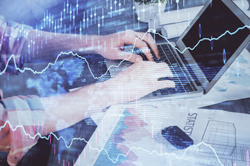 Double exposure of stock graph with businessman typing on computer in office on background. Concept of hard work.