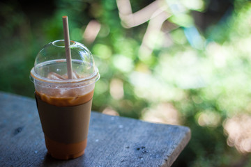 Cold milk tea in plastic glasses on wood table with blur tree background.