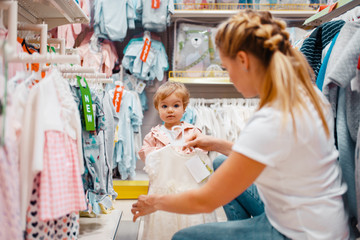 Mother with girl choosing clothes in kids store