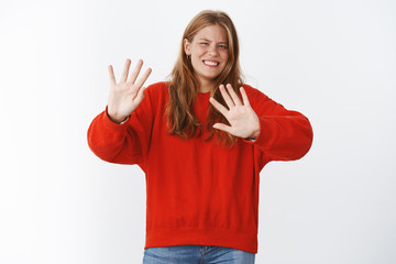 Girl feeling awkward rejecting dumb offer, smiling shy and blushing turning away raising palms in stop and refusal gesture, declining and going backwards wanting to exit over gray background