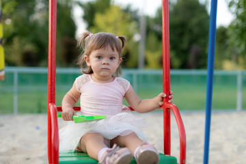 Funny little child, adorable preschooler girl in pretty dress having fun on a swing in the park on summer day