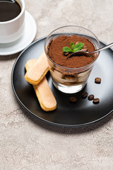 Portion of Classic tiramisu dessert in a glass cup, savoiardi cookies and espresso coffee on concrete background