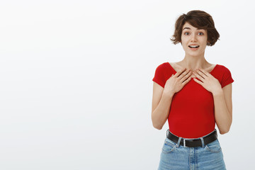 Surprised tender hopeful young cute girl short pixie haircut hold hands chest grateful thrilled look camera faith amusement open mouth winning receive prize achieve goal cheering white background