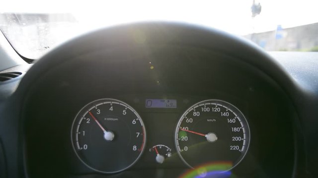 Car dashboard, control panel with speed gauge, fuel consumption during car driving, close up. Focus on gauges, sitter view inside of automobile.Unfocused hands on steering wheel at sun ligth