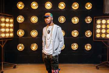 Black rapper in cap on stage with spotlights - obrazy, fototapety, plakaty