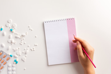 Femаle hand, notepad, pencil, drugs on white background. Flat lay.