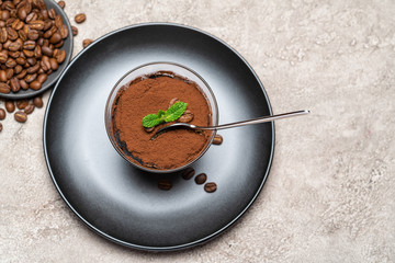 Portion of Classic tiramisu dessert in a glass cup on concrete background