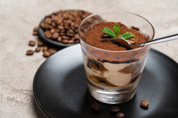 Portion of Classic tiramisu dessert in a glass cup on concrete background