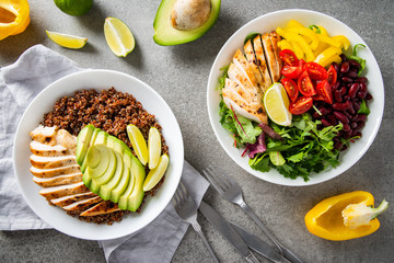 Healthy salad buddha bowl with cherry tomatoes, chicken, beans, sweet pepper, lime and mixed greens and quinoa, avocado, chicken plate on concrete background top view. Healthy food, dish, dinner