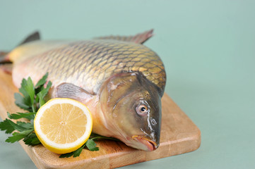 Uncooked carp with lemon and parsley on a wooden tray. Traditional dish for the christmas table. Light background. Close-up. Place for text.