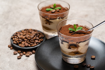 Portion of Classic tiramisu dessert in a glass cup on concrete background