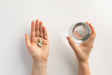 Hands holding a glass of water and pills. Top view.