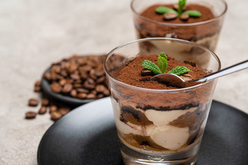 Portion of Classic tiramisu dessert in a glass cup on concrete background