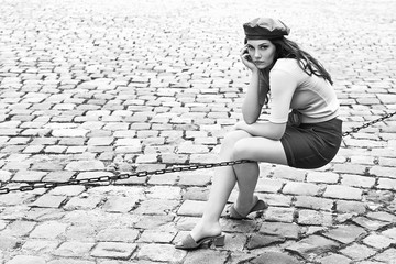 Young beautiful brunette emotional girl dressed in retro vintage style in the old european city sits of a chain