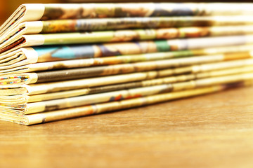 Fototapeta premium Pile of fresh morning newspapers on the table at office. Latest financial and business news in daily paper. Pages with information (headlines, articles, photos, text). Folded and stacked journals