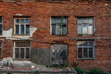 Old grungy wall of red brick with broken windows and wooden door