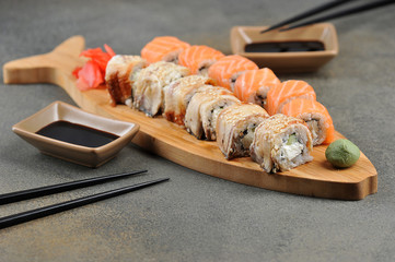 Sushi rolls Philadelphia with eel and salmon on a wooden dish. Bowls of soy sauce and chopsticks. Dark background. Close-up.