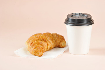 Coffee in a paper cup and a croissant on a light background. The concept of fast food and coffee to go.