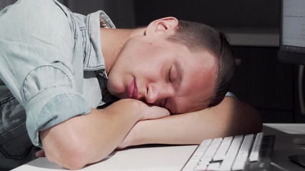 Man sleeping on the table in front of the computer. Sliding cropped shot of a male IT office worker smiling in his sleep, resting on the desk in front of computer. Overworking concept