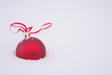 Christmas red ball with a red ribbon on white fluffy snow.